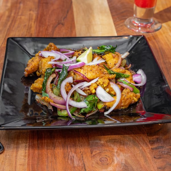 Masthi Bar & Grill's Indian appetizer, featuring crispy fried chicken with red onions, green peppers, and a lime wedge.