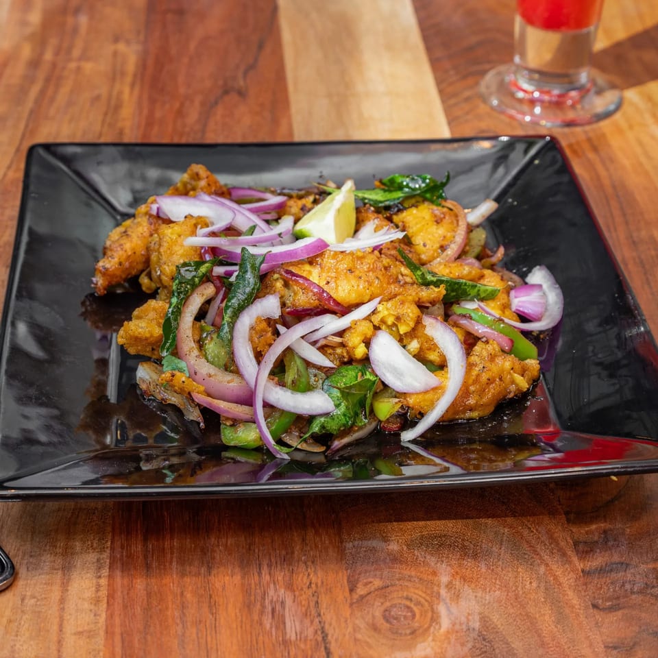 Masthi Bar & Grill's Indian appetizer, featuring crispy fried chicken with red onions, green peppers, and a lime wedge.