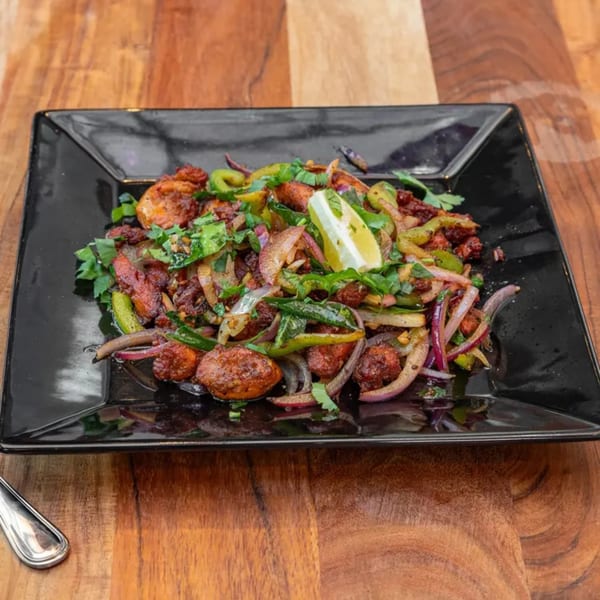 Indian chicken dish with green peppers, red onions, cilantro, and a lime wedge on a black plate.