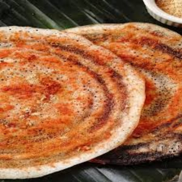 Two golden-brown Indian dosas, speckled with spices, resting on a dark green banana leaf.