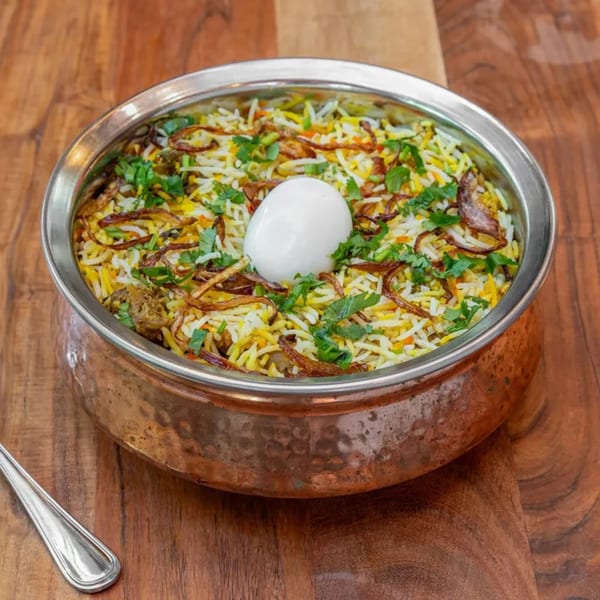 Masthi Bar & Grill's Indian biryani with a boiled egg, fried onions, and cilantro in a copper pot.
