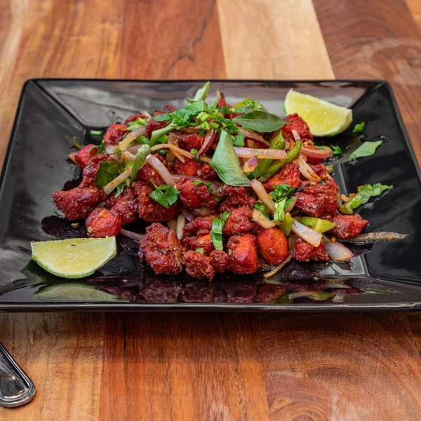 Masthi Bar & Grill's Chicken 65, a vibrant red Indian dish with onions, peppers, and lime wedges.
