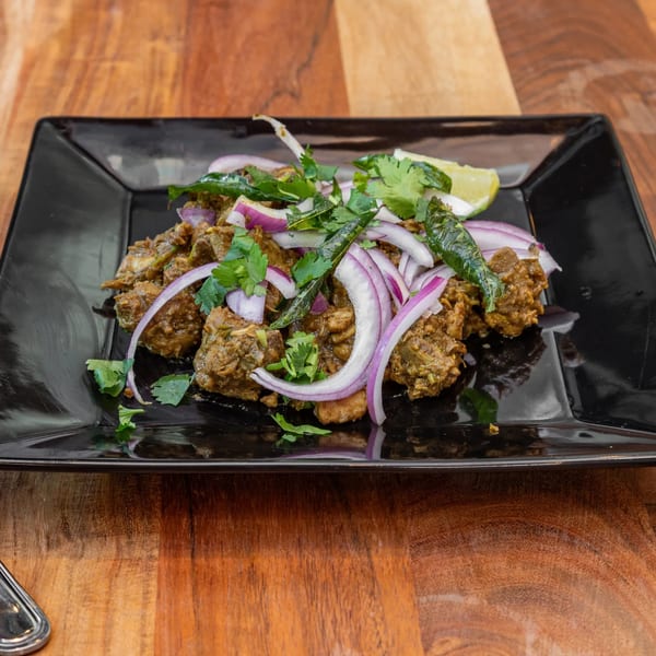 Masthi Bar & Grill's Indian dish with meat, red onions, cilantro, and lime on a black plate.