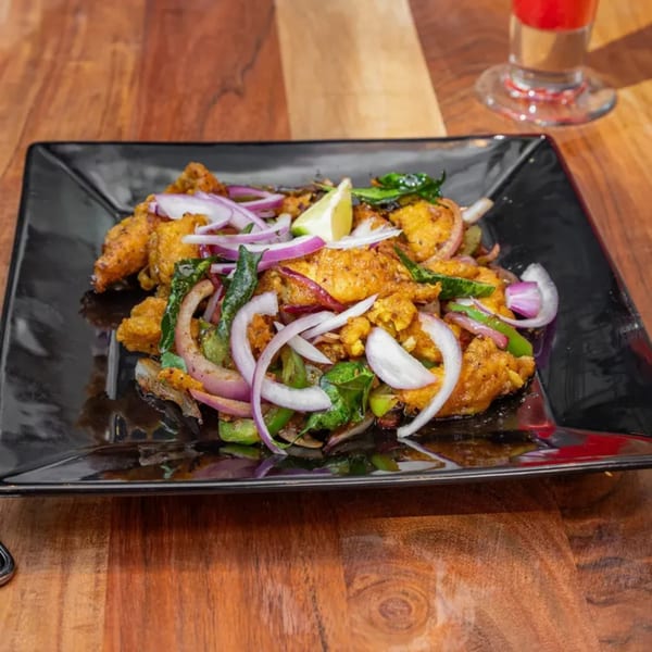Masthi Bar & Grill's Indian appetizer, featuring fried chicken, red onions, green peppers, and a lime wedge.