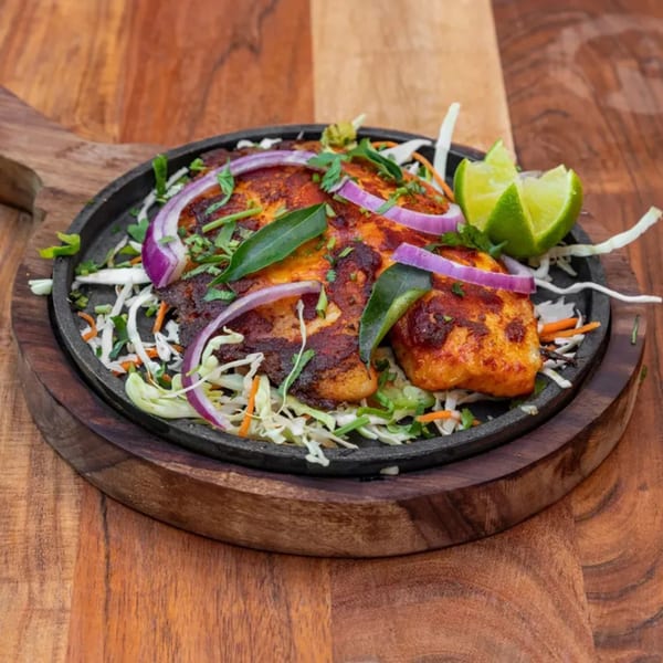 Indian grilled fish with red onions, cabbage, and lime wedges on a sizzling platter.