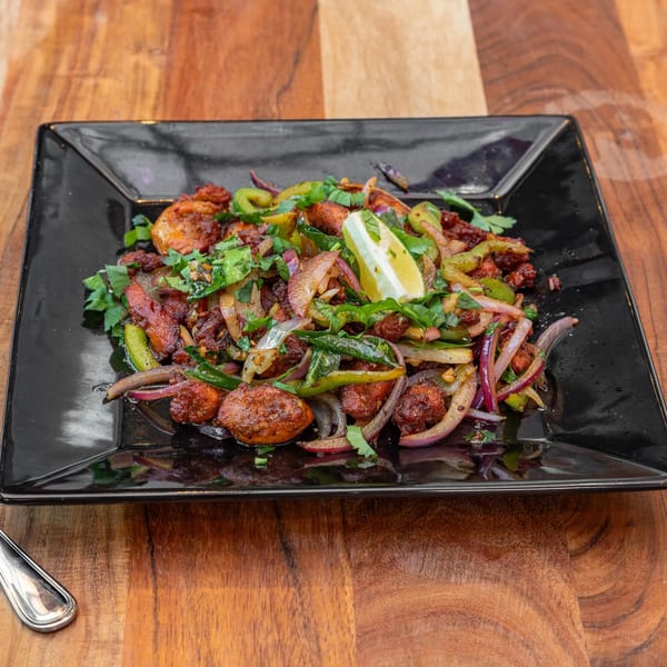 Masthi Bar & Grill's Indian chicken dish with onions, peppers, and cilantro, garnished with a lime wedge.